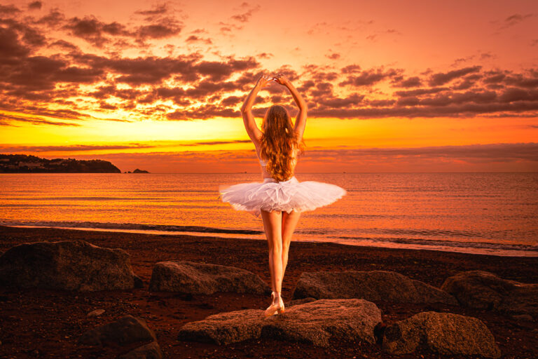 Adult dancer in a ballerina costume photographed from behind at sunrise on a Torbay beach